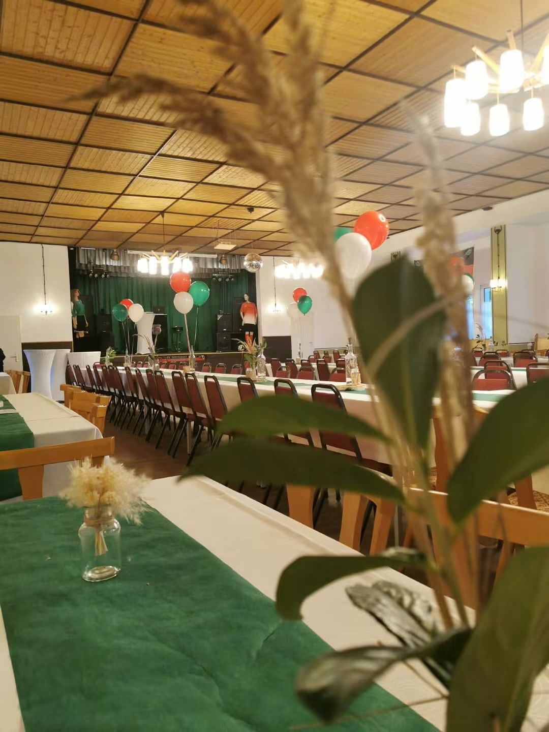 Festlich gedeckte Tische mit grünen Tischläufern und Blumenschmuck im Saal.